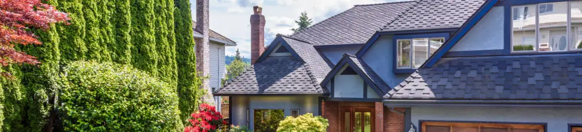 Blue-gray two-story home with a gabled roof behind tall hedges