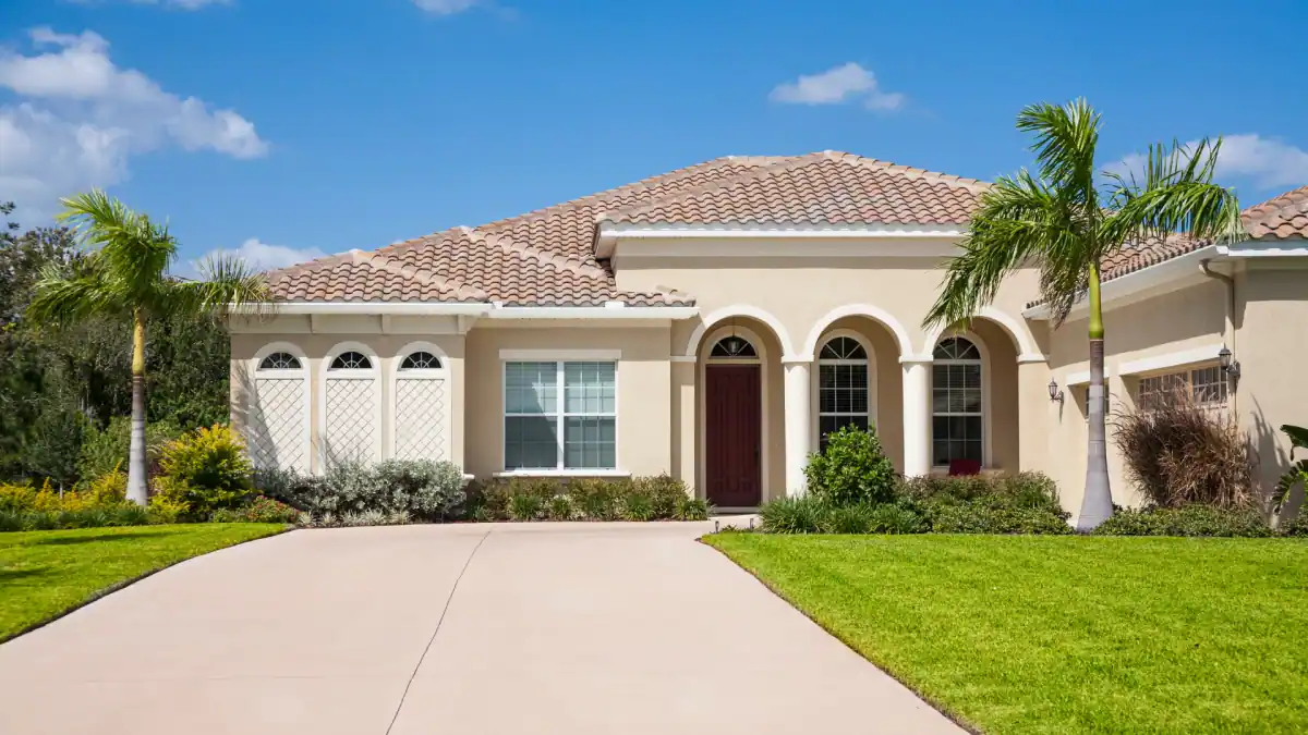 Spanish-style stucco home with a red tile roof, arched entry and palm trees under a blue sky