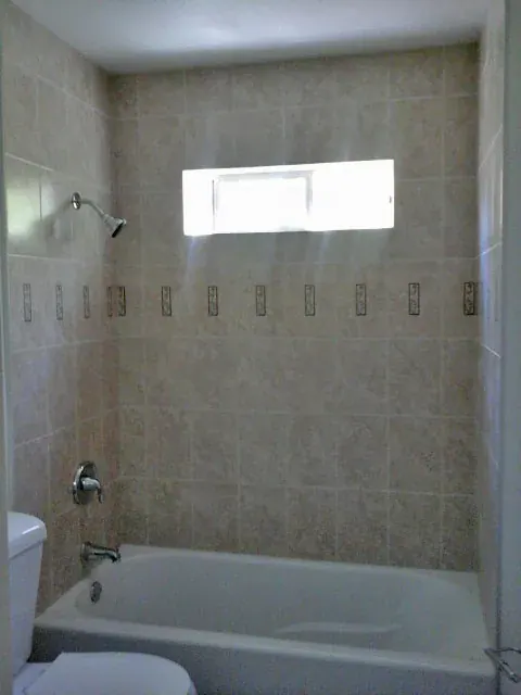 Beige tile tub and shower combination with a decorative border and frosted window