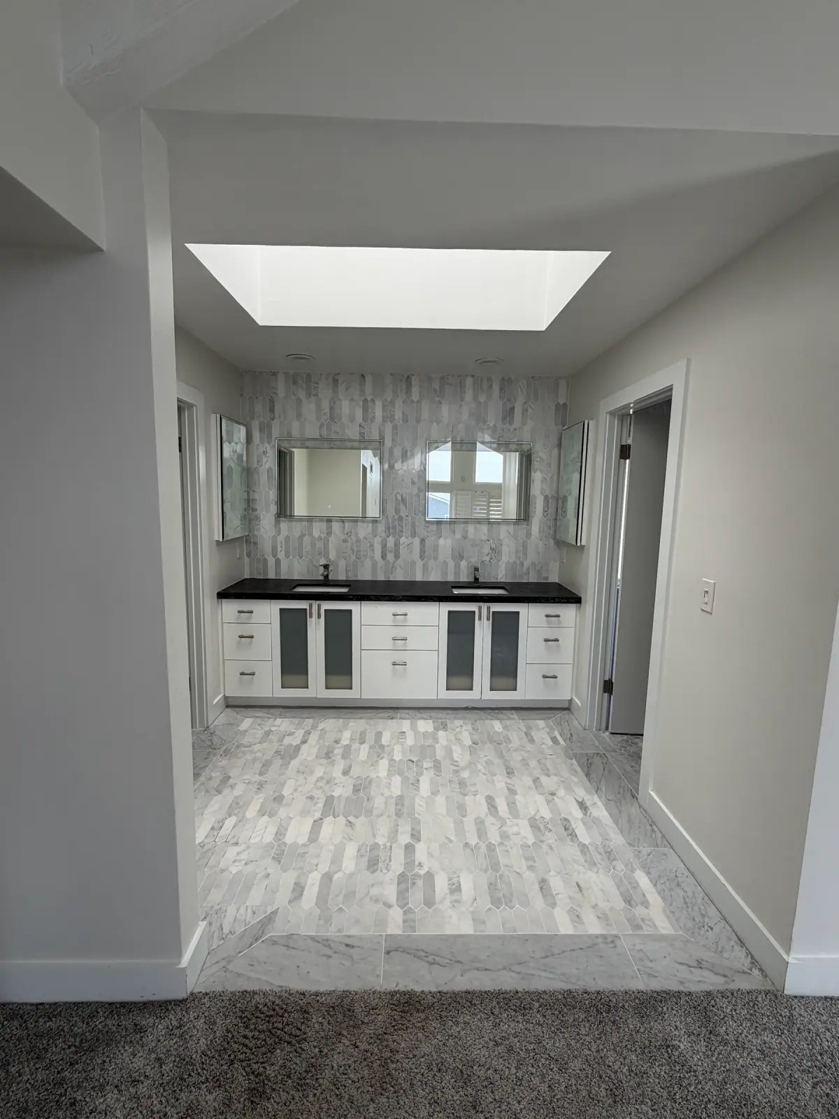 Primary bathroom with a skylight over a white double vanity, black countertop and gray picket mosaic tile on the wall and floor