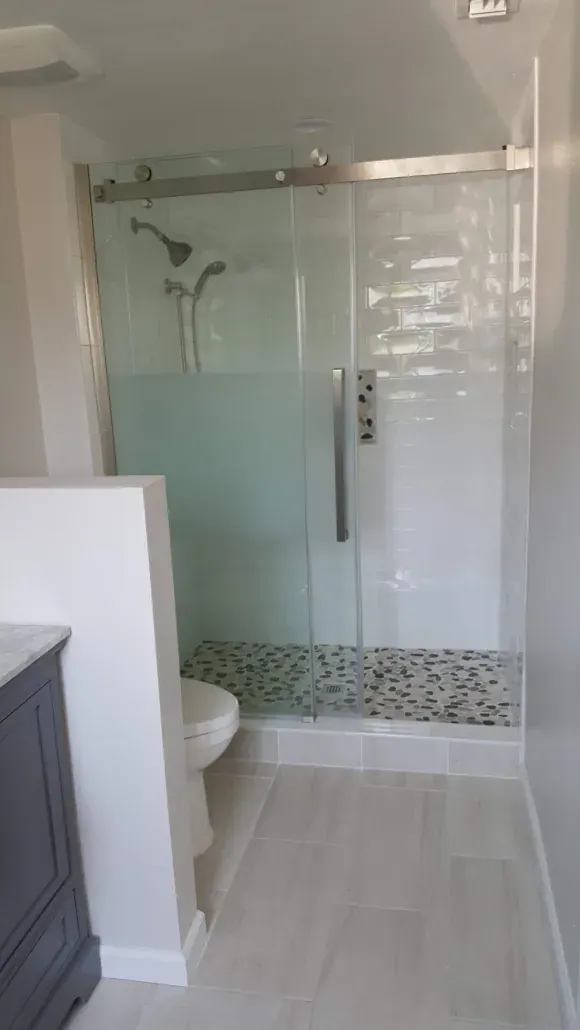 Frameless glass shower door and a pebble-tile accent strip in a remodeled guest bathroom