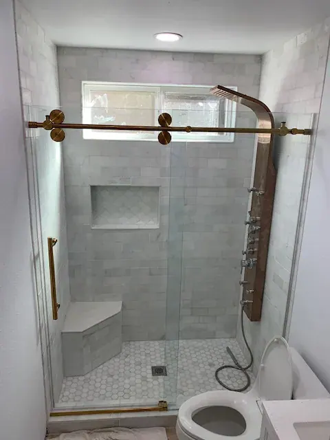 Glass-enclosed shower with a built-in tile bench, recessed niche and brass shower panel