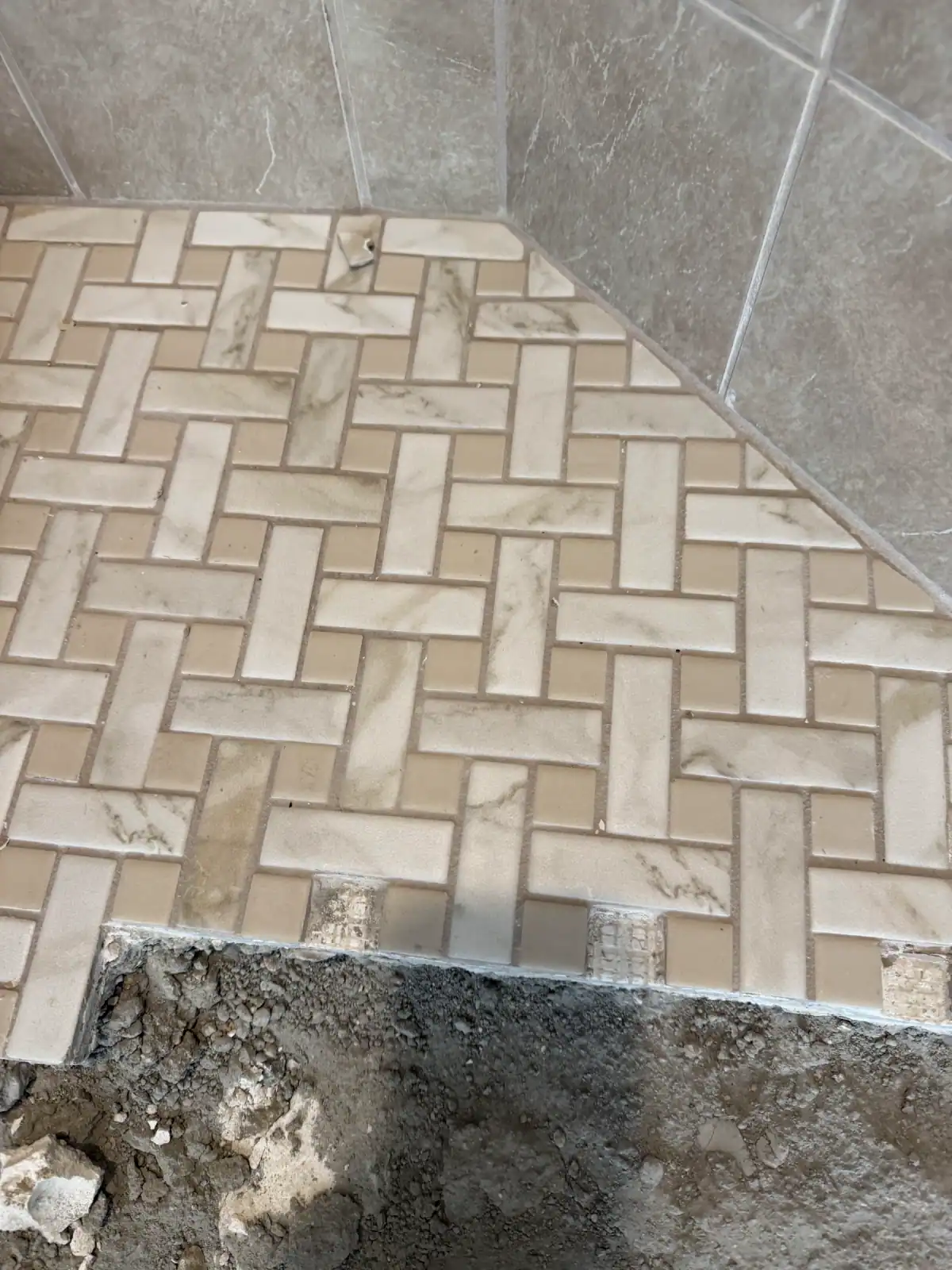 Herringbone floor tile being set next to a shower, with the floor still open in the foreground during the remodel