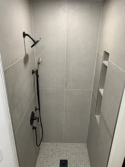 Walk-in shower with large-format gray porcelain tile, a recessed niche and a matte black shower set