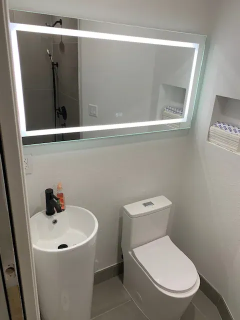 Compact bathroom with a backlit LED mirror, white pedestal sink and one-piece toilet