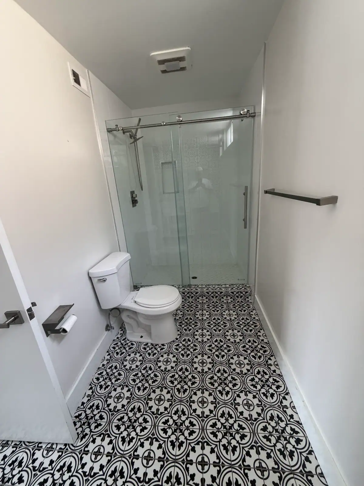 Bathroom with black and white patterned floor tile, a sliding glass shower door and matte gray towel bars