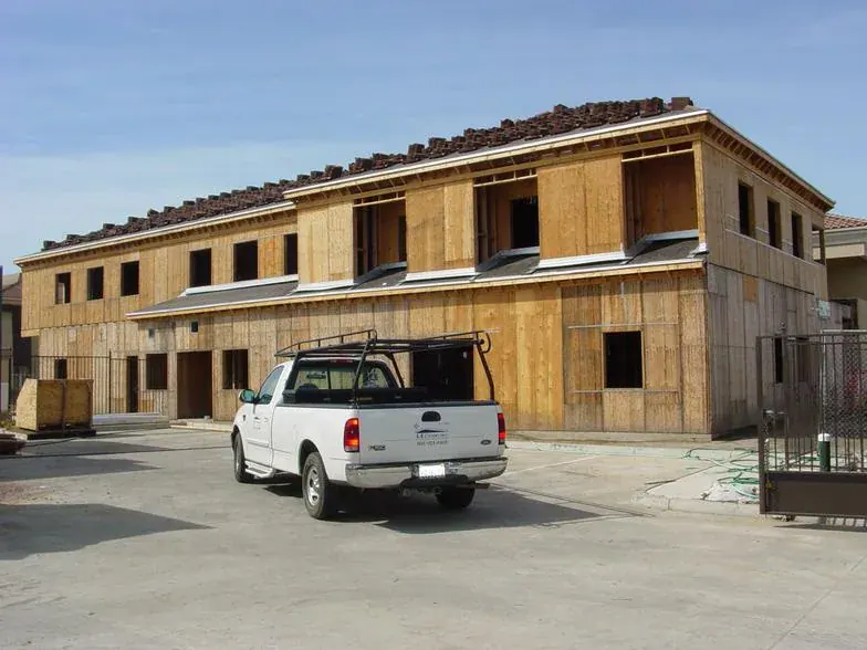 Completed wood framing and tile roof on a long two-story building, with a contractor pickup in front