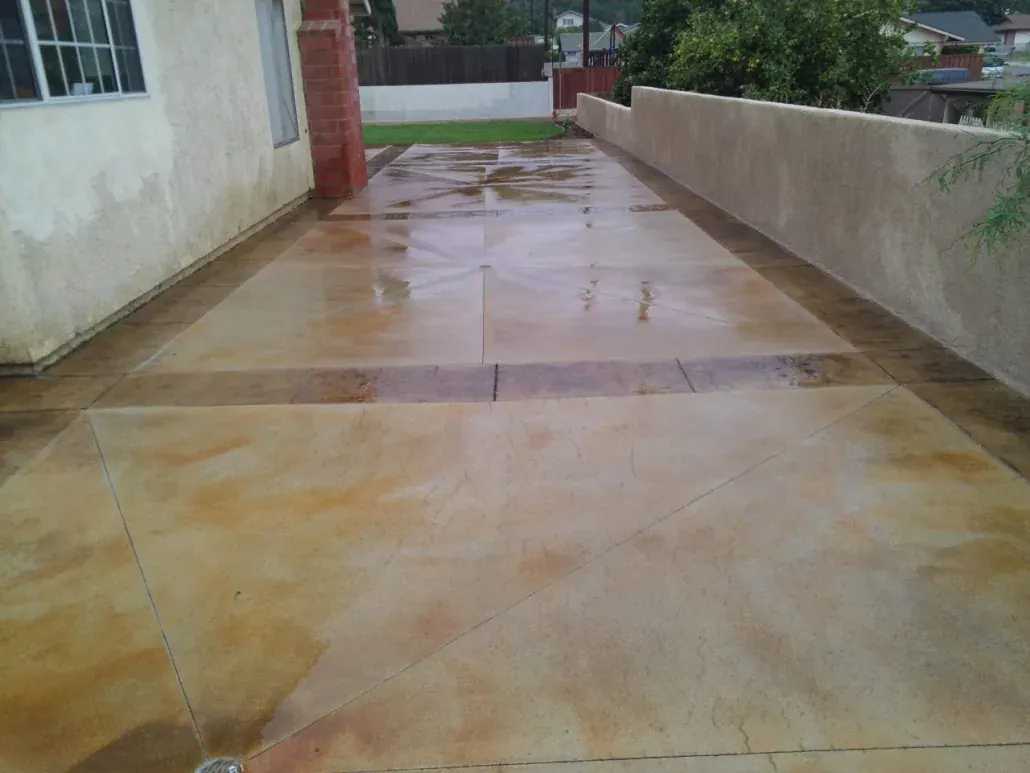 Acid-stained concrete side-yard patio with scored joints running along a stucco house wall