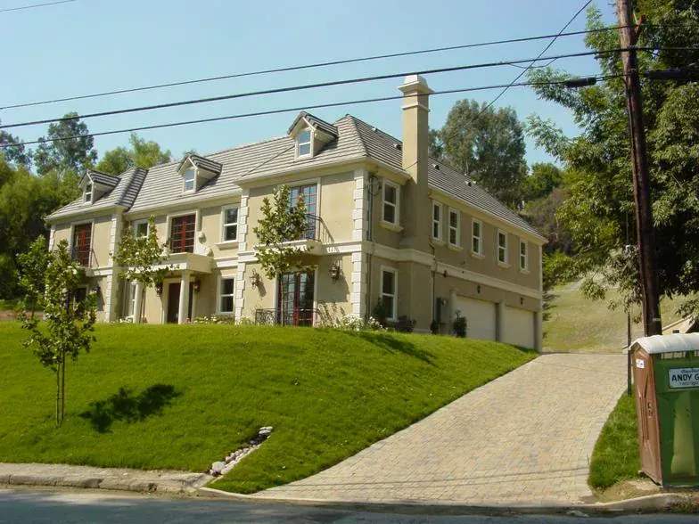 Completed two-story custom home with a gabled roof, stone-paved driveway and new lawn on a sloped lot