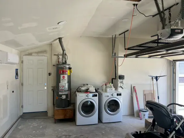 Garage with newly hung and finished drywall on the walls and sloped ceiling, a wall-mounted mini-split, water heater, washer and dryer