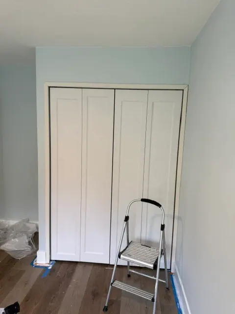 Bedroom with new white bifold closet doors, fresh paint and wood-look flooring near the end of a remodel