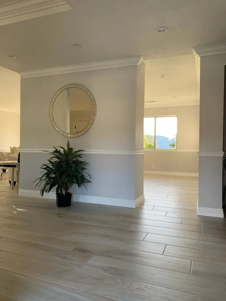 Entry hall with a wide cased opening, round mirror and wood-look tile flooring in a remodeled home