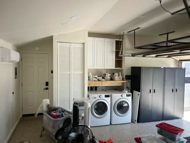 Finished garage with a laundry area, white upper cabinets, a louvered closet, mini-split, flake-coated floor and storage cabinets