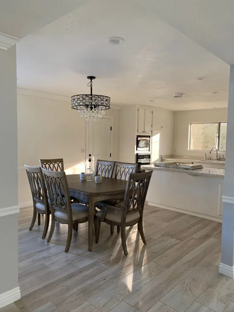 Open dining area flowing into a white kitchen under a vaulted ceiling in a remodeled home
