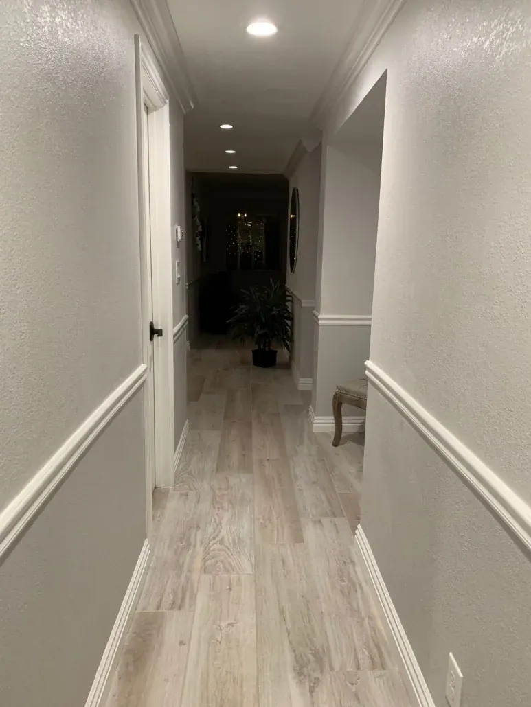 Widened hallway with wood-look tile flooring, chair rail and recessed lights after a whole-home remodel