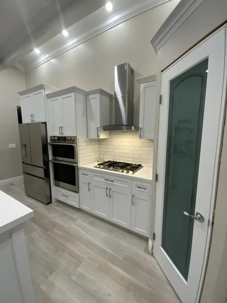 Galley-style kitchen with white cabinets, stainless range hood, gas cooktop and a built-in double wall oven