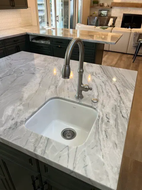 Kitchen island with a white undermount sink, gooseneck faucet and gray-veined stone countertop over dark cabinets