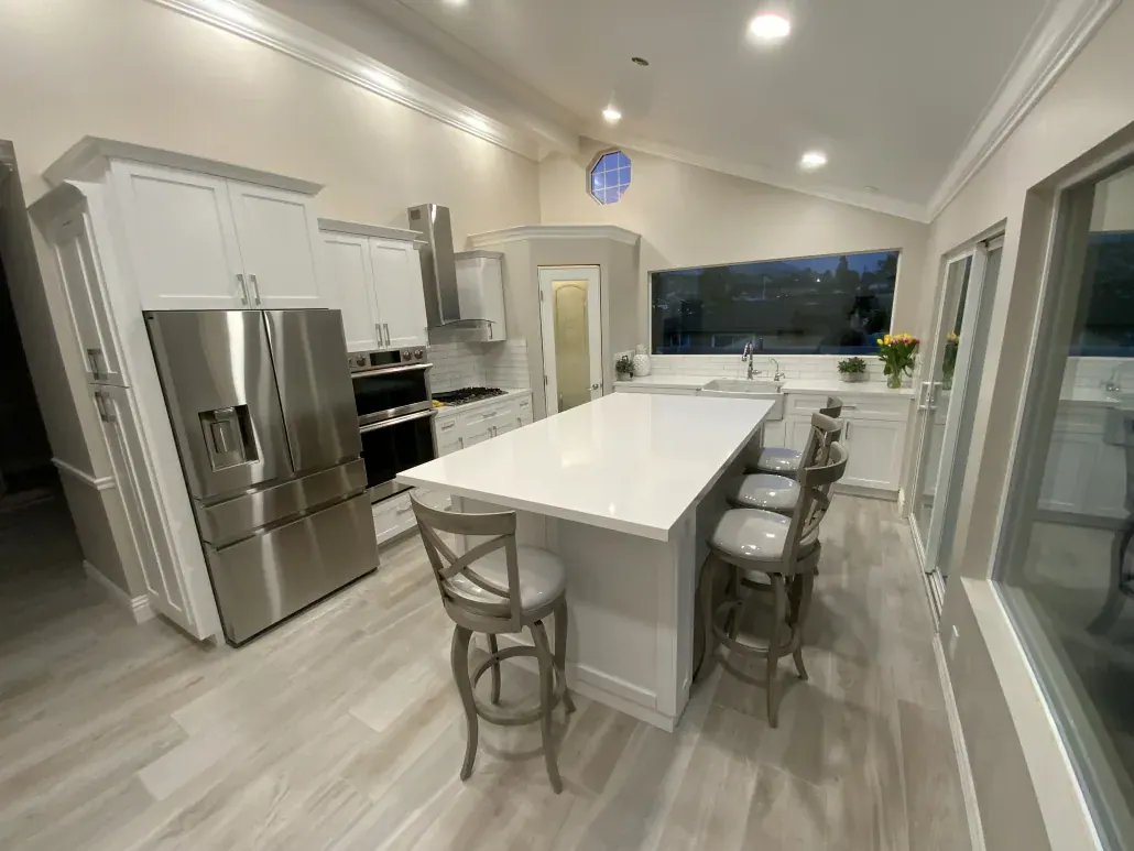 Bright remodeled kitchen with a white quartz island, bar stools, stainless refrigerator and wood-look tile floor