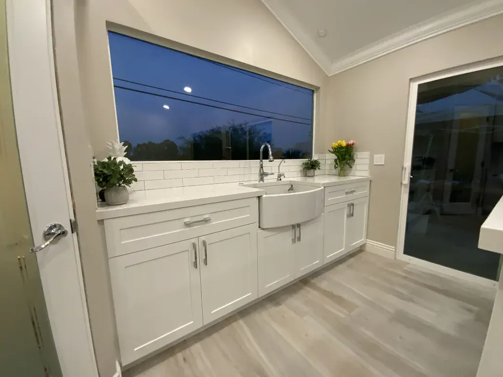 White shaker cabinets with a farmhouse sink under a wide picture window in a remodeled kitchen