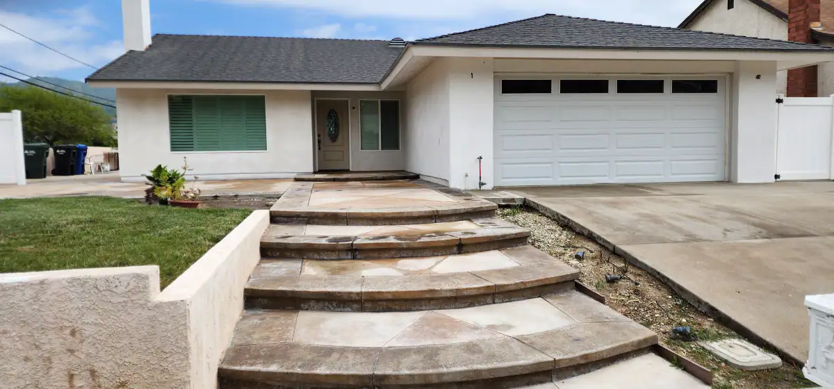 Single-story house after a full re-stucco in a white finish, with a paneled garage door and curved stained concrete entry steps