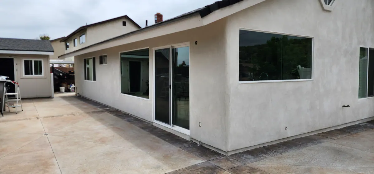 Side of a re-stuccoed single-story house in a smooth off-white finish with large windows and a sliding glass door